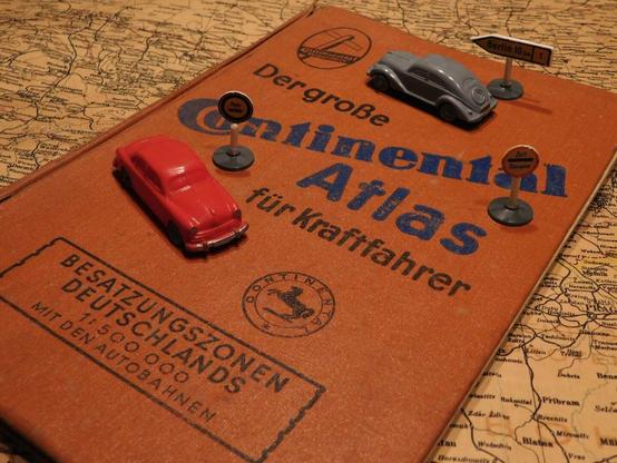 Zwei sehr frühe Wiking-Modellautos, sowie drei Verkehrszeichen, stehen auf dem Cover des "Continental-Atlas für Kraftfahrer" für die deutschen Besatzungszonen.
Unter dem Buch liegt eine alte Landkarte.
