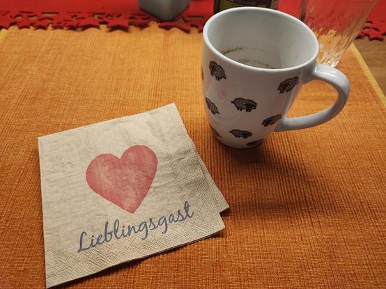 Tasse Kaffee mir einer Serviette mit einem Herz in rot mit der Unterschrift Lieblingsgast.