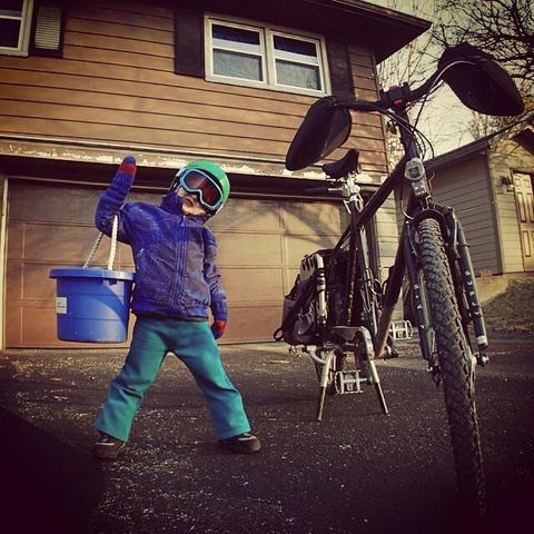4 year old child stands next to cargo bike in winter clothes goggles and mittens. Ready to go!