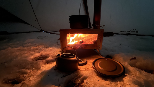 A night shot of the same wood stove. A fire gives a warm light.