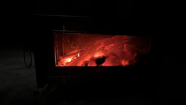 A close of a wood stove window with glowing hot coals.
