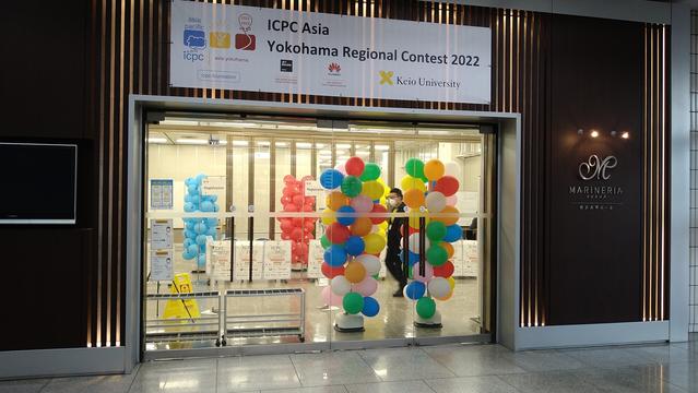 Entrance to the venue of the ICPC contest. A double glass door, with colorful balloons behind it, and a large white banner on top announcing the contest.