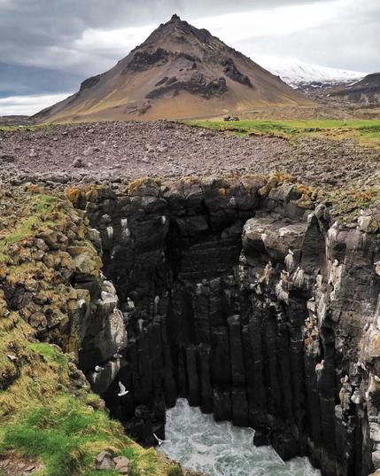 A pyramid-shaped mountain in the background and a big, basalt bore hole in the foreground.