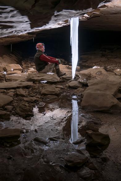 Person in red looks at an ice formation, their reflections on the ice pond