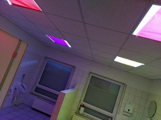 Blick in einen Waschraum. Die Rollläden sind unten, die quadratischen deckenlampen mit bunten Farbfolien verhängt.