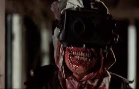 A new scarecrow with no lips and bloody face with giant black goggles on and a rag on his head.