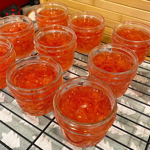 Jars of bright peach-orange jam without lids on cooling rack.