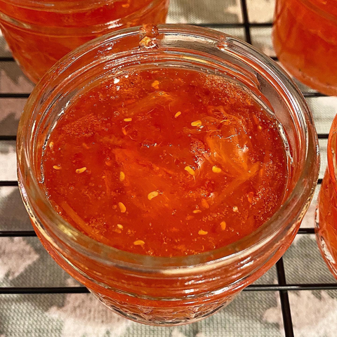 Jar of bright orange-peach jam with no lid to show texture of fruit chunks, seeds, and peel.