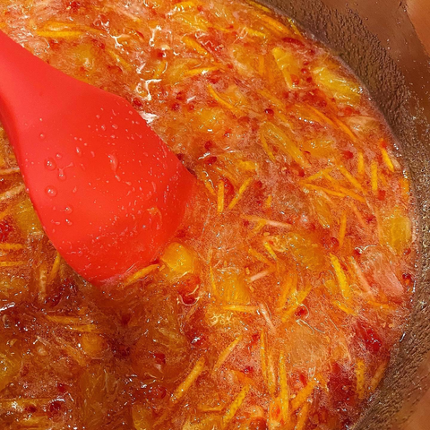 Oranges, lemons and raspberries chopped and reducing in a pot with sugar stirred with a red spatula.