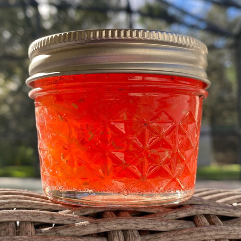 Jar of jam sitting on wicker chair in natural sunlight to enhance color.