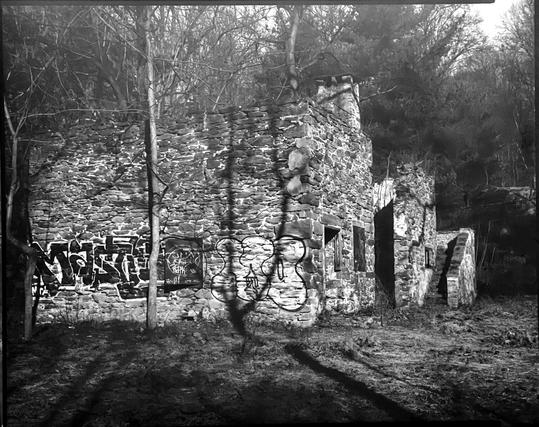 The ruined barn in black and white, generally dark, with graffiti on the wall facing the camera, and steps going up to a non-existent second level.