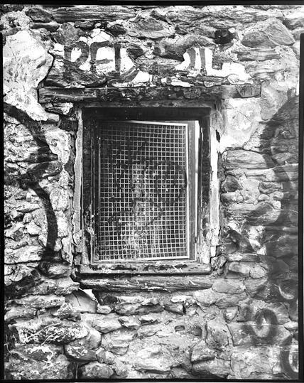 Detail shot of one of the windows/Metal access hatches from the inside of the barn. The wall is covered in graffiti and the masonry is all crumbling.