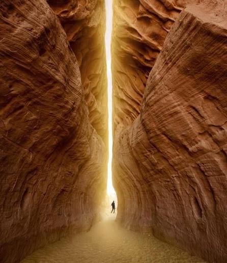 Image is a colour photograph. The entire photo is mountain cliff with one gap in the middle that lets in the light. A figure is standing in the gap