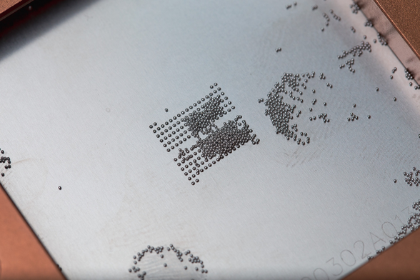 BGA reballing: A lot of solder balls on top of a metal stencil.