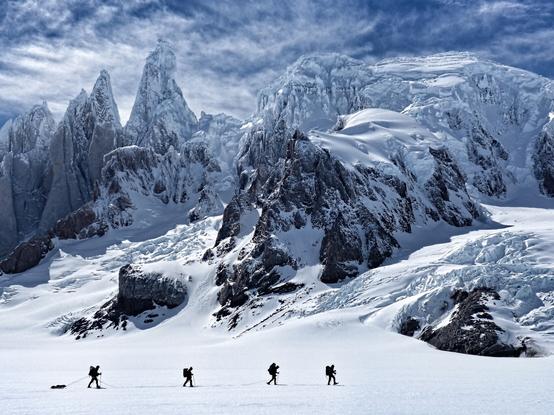 4 men walking across a glacier with a backdrop of ice and mountains in Patagonia. Cerro Torre range