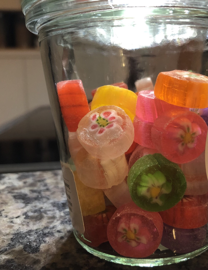 Colorful, translucent hard candies that look like Venetian glass in a clear glass jar. Each one looks like it has a little flower captured inside of it.