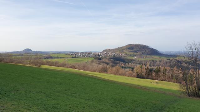 Bild zeigt links und rechts zwei Kaiserberge, im Vordergrund grüne Wiesen. Auf dem rechten Berg steht eine Burgruine und eine Kirche.
