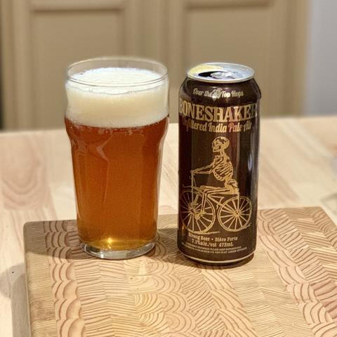 A can of Amsterdam Boneshaker beside a nonic glass full of the same, with an inch of off-white head and a slightly hazy copper colour.