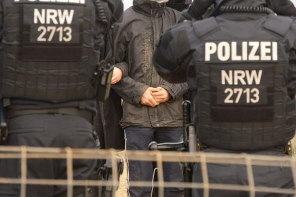 Polizisten stehen vor einer Menschenkette, die Menschen haben sich untergehakt.