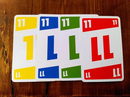 Four cards of the game phase 10, all with the number 11 on it. The colors from left to right are yellow, blue, green and red. The yellow card is barely readable because of bad color contrast. 😢