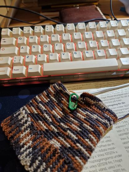Pic got a little wide but is showing a tube of yarn in black, brown and beige. It's on a messy desk.