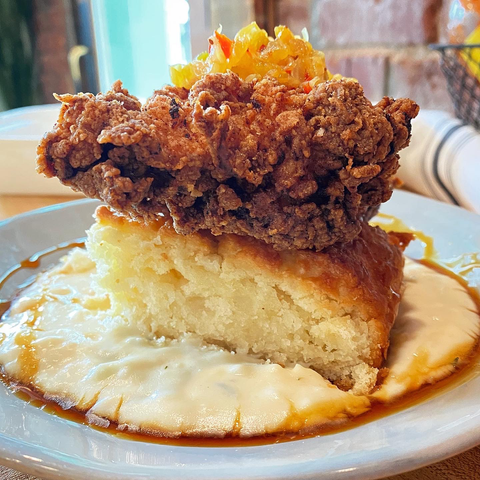 Fluffy biscuit topped with fried chicken thigh and chow chow on creamy sorghum and syrup