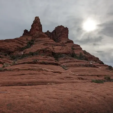 The Bell Rock formation in Sedona. 

Layers of red form a butte, which looks like a bell from certain angles. The sky is a haze of clouds, but the sun is breaking through in the top right corner.