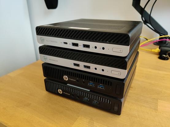 Four HP Prodesk Minis machines stacked on top of each other on a desk, front view.