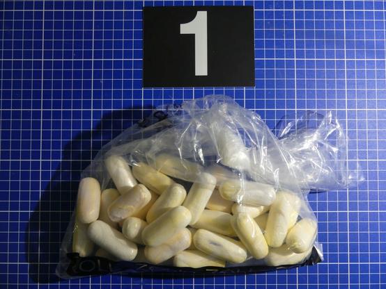 In einer durchsichtigen Plastiktüte sind sogenannte Fingerlinge mit Kokain enthalten. Ein Mann hatte 51 Stück davon im Körper geschmuggelt (500g). Über der Tüte liegt auf dem Tisch eine Ziffer "1" als Beweisstückmarkierung.