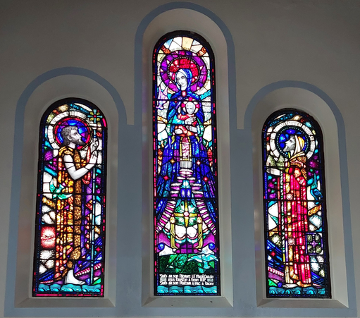A three panel stained glass window. The centre panel shows the Virgin Mary holding the infant Jesus.