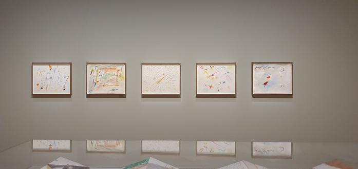 Exhibition View: five large scale colourful drawings in a row, in the foreground mirrored by a glass case.