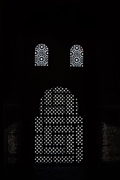 Mostly black and white, symmetric picture of medivieal arab windows, a big window at the bottom, and two smaller ones at the top. The impression is that of a face with an open mouth. The windows are arched and filled with patterned woodwork.