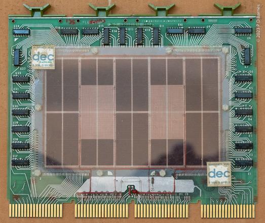 Front view of an 8k memory board from a PDP11 computer. Most of the board is taken up by the cores, which from this distance are individually indistinguishable, and just form brown rectangles. Protecting the cores is a perspex sheet, on which are two stickers reading "Warranty void if broken". The stickers are unbroken, but the warranty's probably void anyway. Surrounding them are a number of old-style black plastic "caterpillar" 14 pin LSI chips. Across the top of the board are four plastic handles for insertion and removal, and across the bottom are four groups of gold-plated contacts for insertion into the computer's Unibus, or communication bus.