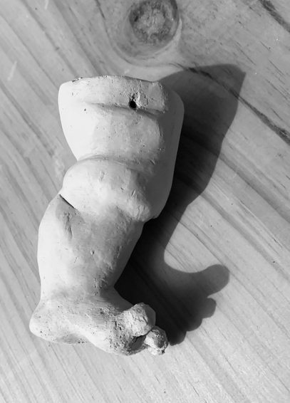 black and white photograph of a doll's leg modeled from clay.  it is planned as a part for a mobile with doll body parts and therefore has a small hole at the top edge for hanging.  the leg is fleshy and thick and has a short, wide foot with rounded, splayed toes.  picture 3: side view of the inside