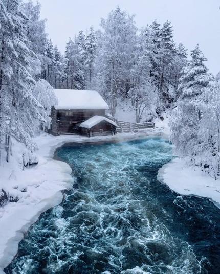 Finland.
Winter.
The forest river did not freeze.
There is a cozy warm house on the bank of the river.
Beautiful nature.