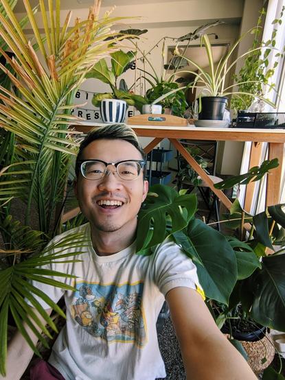 Cute single Asian guy with glasses with highlights and a Pokemon t-shirt surrounded by house plants.