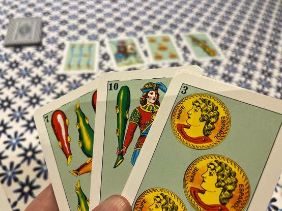 A hand holding three Spanish deck card, the one on top a three of golds