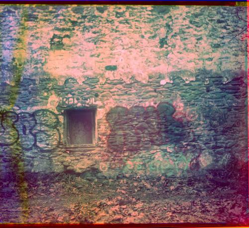A color image made by combining 3 filtered black and white images recorded on color-sensitive paper. Shows a stone wall and a window covered in graffiti.