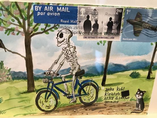 Bemalter Briefumschlag mit einem Skelett auf einem Fahrrad in einer grünen Landschaft mit Bäumen und einer kleinen Katze in der Ecke.