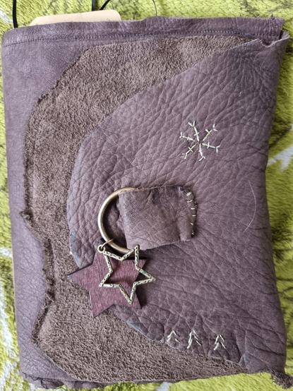 A raggedy looking book cover made from a faux leather handbag, with a metal and wooden star attached to it. The fake leather is brown, and there are small embroidered details on it: three small fir trees and one snowflake.