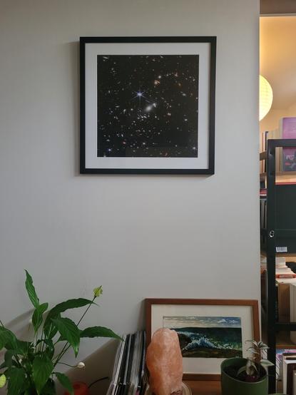 Framed print of the first deep field image taken by the James Webb Space Telescope. On a side table below sits two plants, a salt lamp, and vinyl records.
