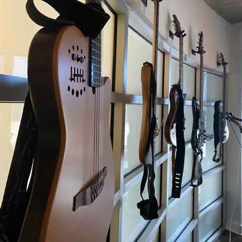 A Godin acoustic-electric nylon string, a Warmoth strat, a Fernandes Ravelle, a Music Man Bongo 5 bass, and an Ibanez 5 string bass hanging on the wall.