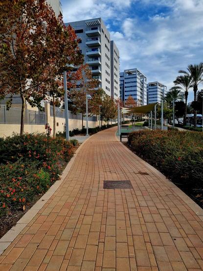 A paved path leading up, alongside white and grey apartment buildings under a partly cloudy sky