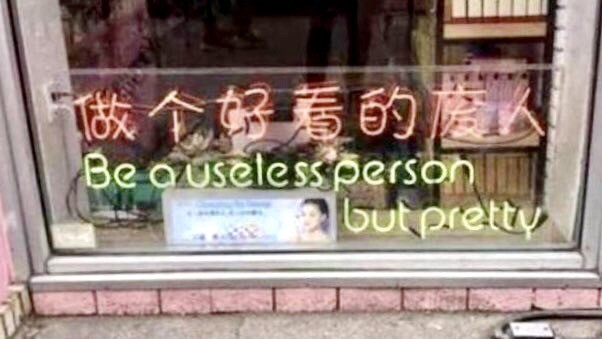 Neon sign with Asian characters and “Be a useless person but pretty” beneath them.