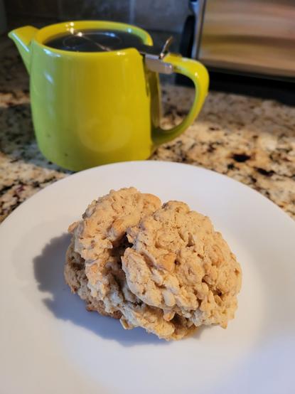 Oatmeal cookies on a white plate with a green teapot behind.