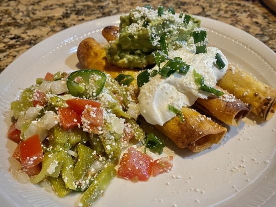 Taquitos garnished with guacamole and sour cream, plus a cactus salad on the sidez