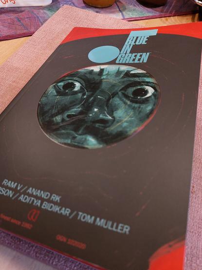 Das Cover von "Blue in Green" ist gezeichnet und zeigt eine vinyl Schallplatte vor rotem Hintergrund. Das Label zeigt ein Gesicht mit entsetzt startenden Augen. Die Schallplatte scheint im unteren Bereich zu zerfließen.