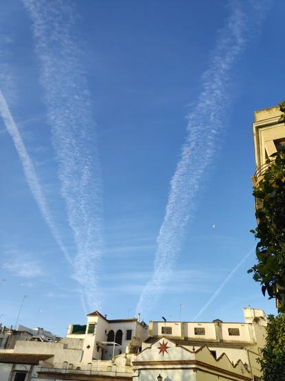 En la parte inferior y a la derecha se ven fachadas de casas de pueblo. En el cielo, azul, se ven varias estelas de aviones, que se han expandido y se han convertido en cirrocúmulos. También se ve la luna menguante en la foto y otros cirros por el fondo, mucho más transparentes.