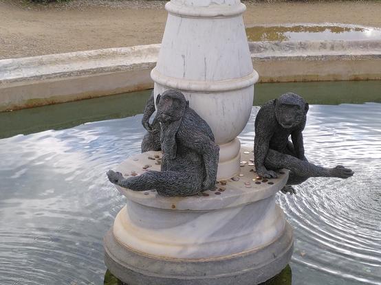A sculpture of two monkeys sitting on a marble pedestal in the middle of a large fountain.