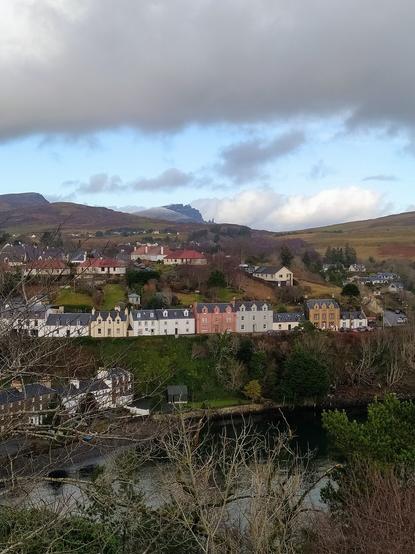A portrait oriented view of colourful seaside houses in the bay of Portree with the Old Man of Storr just visible on the horizon above